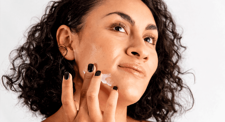 A woman is looking up and to her right as she rubs cream onto her jaw.
