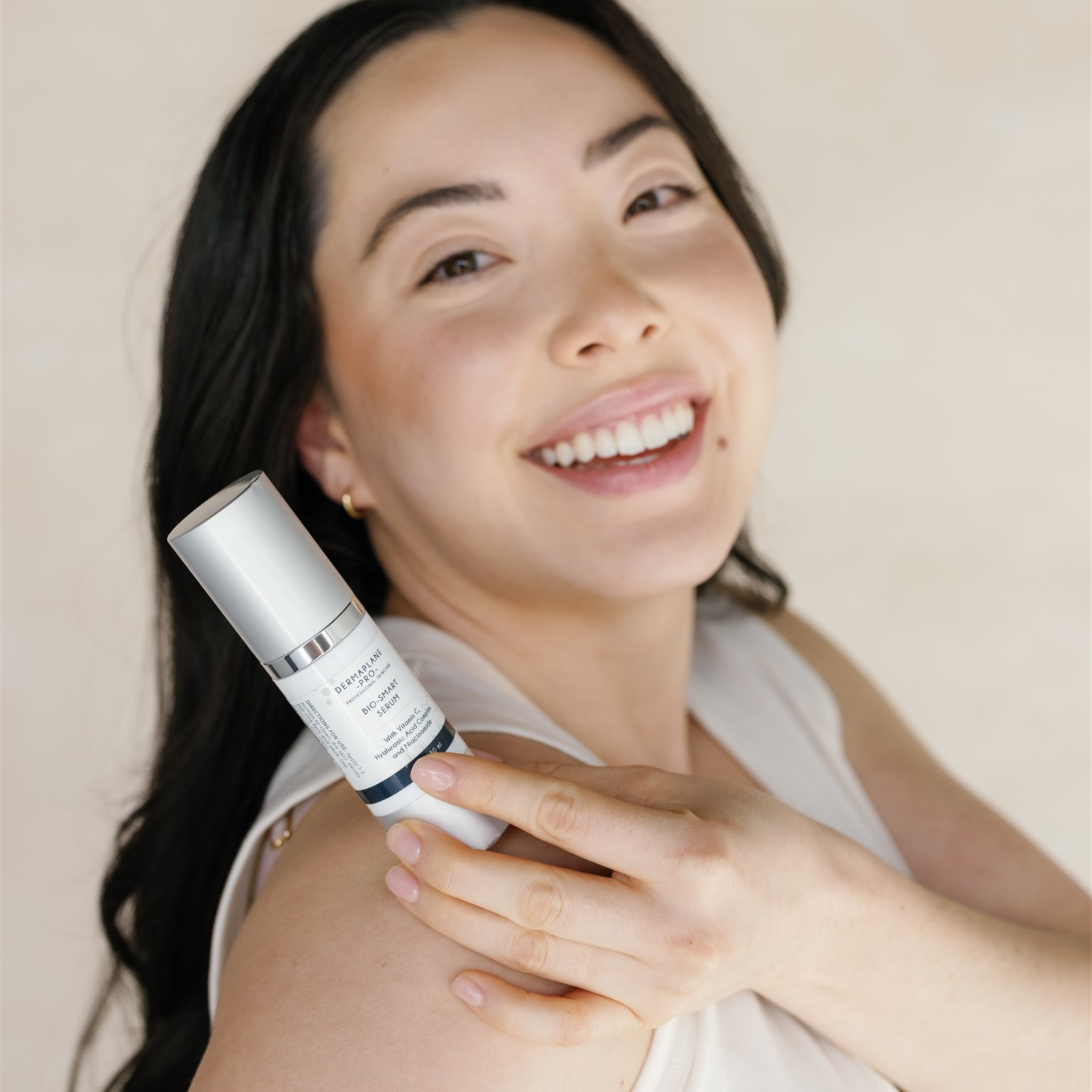 A smiling young woman holding a bottle of DermaplanePro's Bio-Smart Serum.