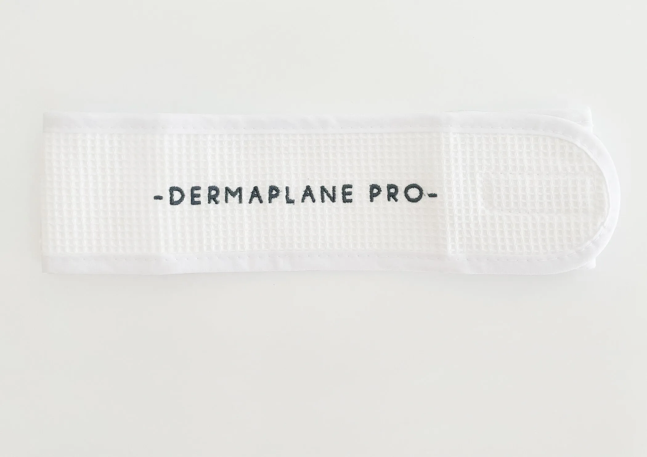 web-dermaplanepro-Headwrap-HERO DermaplanePro waffleknit headwrap with velcro closure and navy blue logo on white fabric.