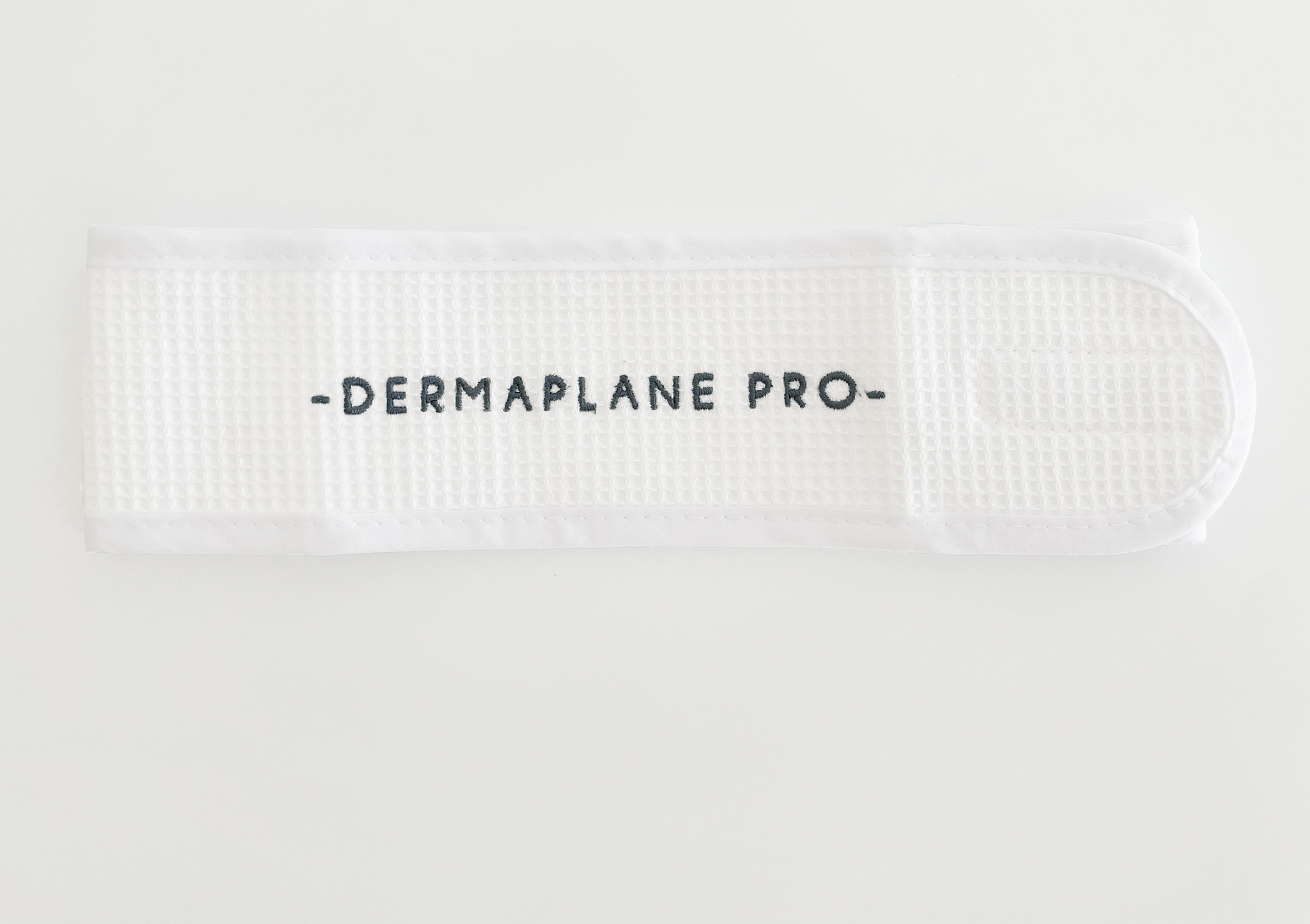 DermaplanePro waffleknit headwrap with velcro closure and navy blue logo on white fabric.